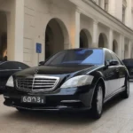 A diplomatic car, likely a Mercedes-Benz S-Class, is parked in front of a luxury hotel in Geneva